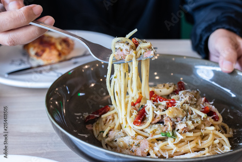 Fork lifting spaghetti aglio e olio with bacon dried chili and parmesan cheese from deep bowl. (