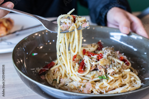 Fork lifting spaghetti aglio e olio with bacon dried chili and parmesan cheese from deep bowl. (