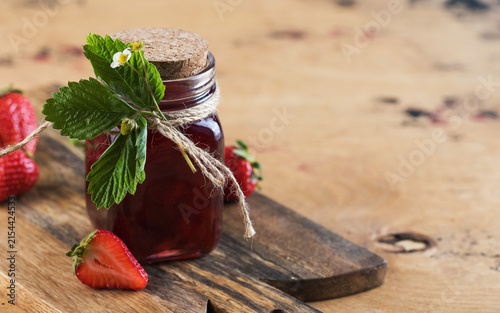 Homemade strawberry jam in glass jar with fresh strawberries on rustic wooden board