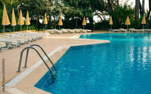 Outdoor swimming pool with blue water, empty sun loungers and yellow striped umbrellas. Luxury resort hotel relaxation zone, summer vacation concept.	
