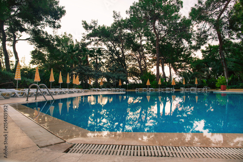Outdoor swimming pool with blue water, empty sun loungers and yellow striped umbrellas. Luxury resort hotel relaxation zone, summer vacation concept.	
