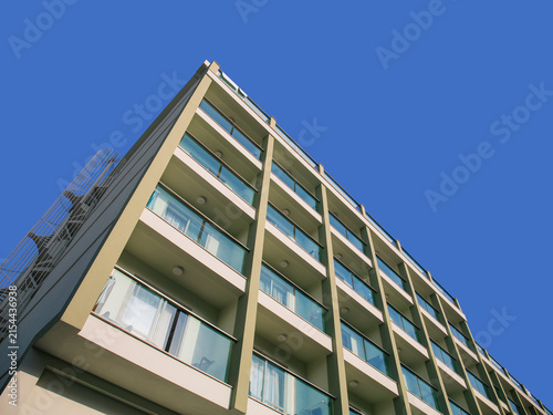 Modern hotel building facade with balconies behind lush green palm trees. Summer vacation resort concept, tropical holiday accommodation.	
