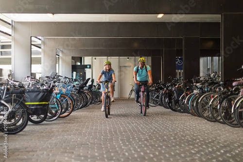 Couple cycling with helmets through a bicycle parking garage