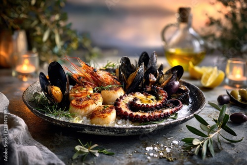 gourmet mediterranean seafood platter with grilled octopus, scallops, prawns and mussels served with lemon, olives and olive oil at sunset
