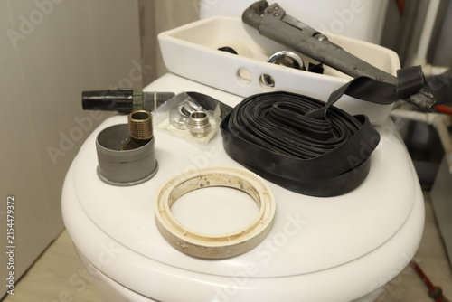 Fotografie Plumbing tools and replacement parts lying on a white toilet lid during a bathroom repair process