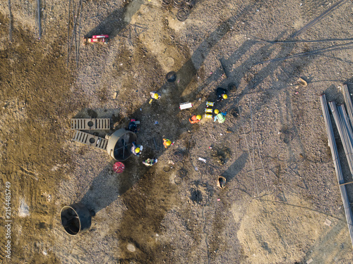 Aerial view of workers in hard hats at the Waste to Energy Facility Construction Project with construction materials on the dirt ground in Kecamatan Denpasar Selatan, Bali, Indonesia.