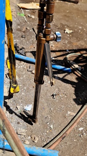 Close-up of an industrial oxy-acetylene cutting torch with gas hoses resting on a rugged construction site.