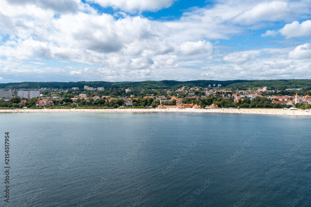 Fototapeta premium An aerial view shows the coastal town of Sopot in Poland, featuring a sandy beach, buildings along the shoreline, and the Baltic Sea.