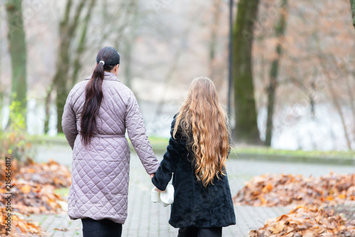 Konstfotografi Mom and daughter walk hand in hand along a path strewn with leaves in an autumn park