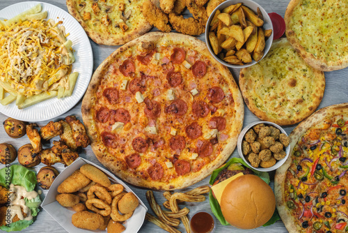 Overhead view of assorted pizza and fast food feast with burger, chicken wings and fries.