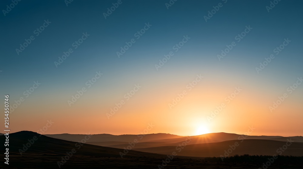 Fototapeta premium Vibrant sunset over rolling hills landscape with gradient sky and silhouetted mountains
