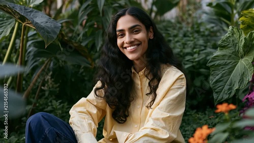 Relaxed woman seated in dense greenhouse foliage with yellow shirt for natural portrait background and wellness banner design