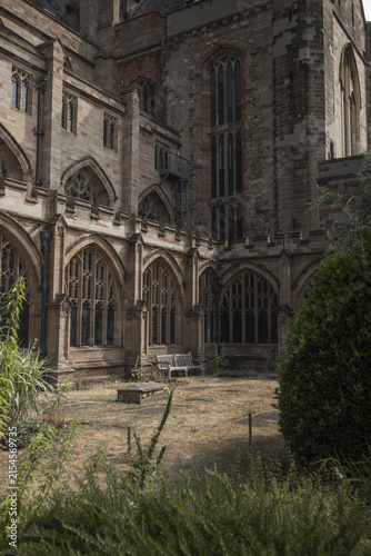 View of the historic stone cloisters and gothic architecture of Worcester Cathedral with a quiet courtyard and lush greenery in Worcester, England, United Kingdom.