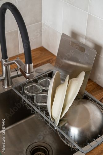 Kitchen with stainless steel sink and contemporary black faucet, dishes and cutlery being washed by hand, neatly stored in dish rack. Manual dishwashing, organization, practical storage, modern design