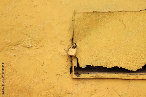 Abstract close-up of a yellow padlock attached to an aged yellow wooden surface