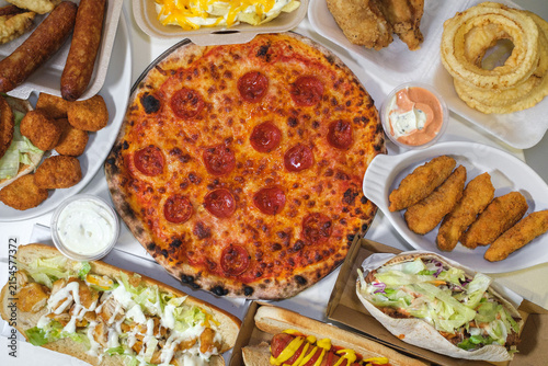 Pepperoni pizza surrounded by assorted fast food and takeaway dishes