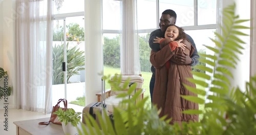 African American couple moving closer, hugging, laughing by suitcase at home, reuniting after trip
