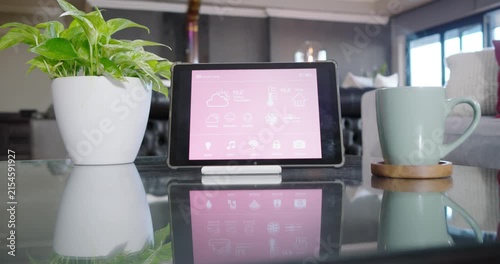 Camera is moving, focusing on tablet on glass table with plant and mug, showing pink reflection