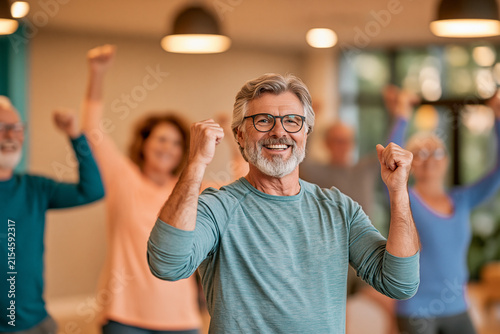 A group of cheerful active seniors participate in a fitness class smiling and pumping their fists in the air with enthusiasm and positive energy
