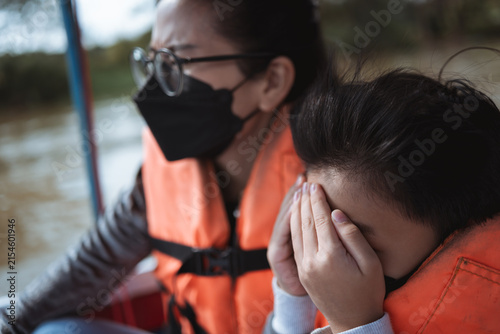Asian mother and son riding a speed boat while wearing life vest and face mask. Parent and child enjoy river trip in countryside.