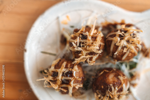 Takoyaki balls topped with bonito flakes and drizzled with sauce on a white plate.