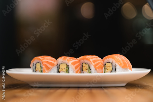 Fresh salmon sushi rolls served on a white plate, beautifully styled with a dramatic blurred background.