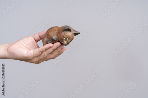 Hand holding a carved wooden cat figurine in a playful pose against a plain background.