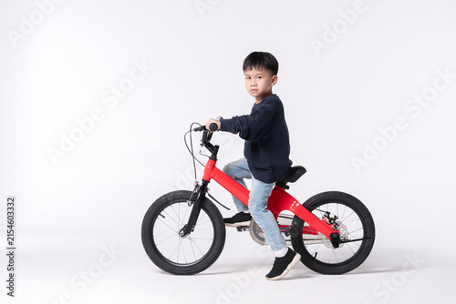 Serious looking Asian child riding a red bicycle in a studio setting.