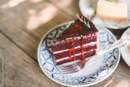 Slice of rich chocolate cake topped with glossy red syrup and garnished with herbs, served on a decorative plate with a fork on a rustic wooden table.