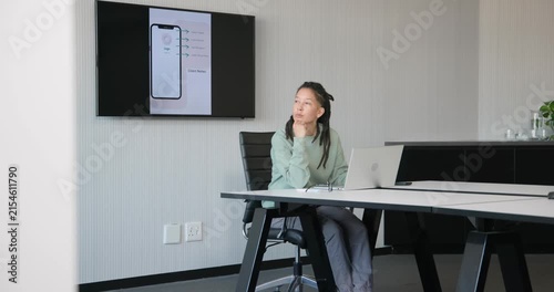Non-binary adult African typing on laptop at meeting table pausing after seeing wall phone mockup