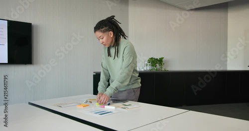 Nonbinary African American reading sticky note arranging neon pads and tablet at table preparing