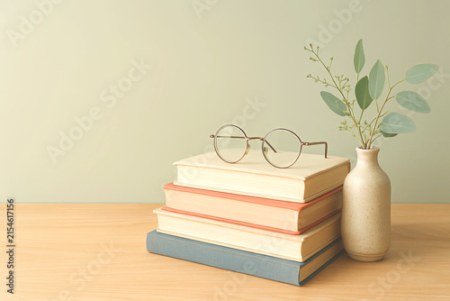 Eyeglasses on a book and a flower vase on a work desk.