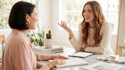 Two creative women discussing ideas at a marble table in a bright studio, perfect for design agency marketing and female entrepreneurship.