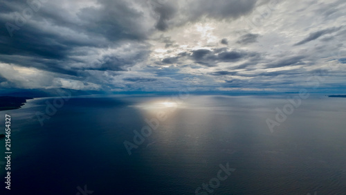 Stormy seascape beneath dramatic clouds. Sunlight breaks through the clouds, creating a luminous reflection on the ocean surface.