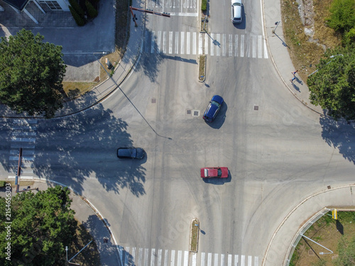 Vehicles navigating through an urban intersection from an aerial drone view. Aerial drone shot of cars driving through a city intersection.
