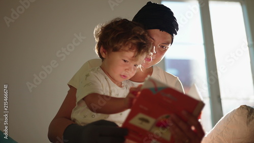 Fotografie Excited toddler reacts joyfully as his mother reads a picture book and kisses hi