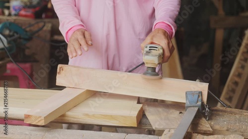 Carpenter's hands using an electric orbital sander to smooth a wooden plank in a woodworking workshop, part of the furniture making and finishing process.	