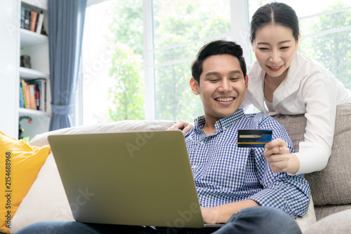 A happy young couple sitting together at home while shopping online and paying with a credit card on a laptop.