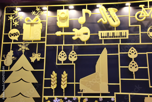 Yellow silhouette artwork featuring a Christmas tree, wrapped presents, snowflakes, guitar, trumpet, piano keyboard, and bicycle on a dark background arranged in a geometric grid.  