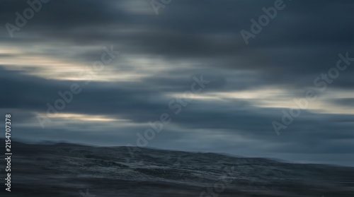 Fotografie Dark storm clouds moving horizontally across moody gray sky with streaking motio