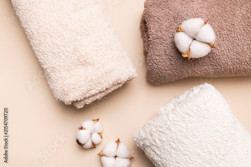 Rolled cotton towels and cotton flowers on beige surface present soft bath textile styling. Plush fabric  natural detail and neutral tones suit spa branding  hospitality visuals and home wellness.