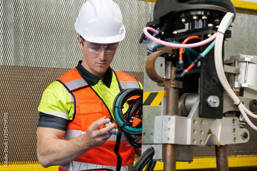 Caucasian male industrial engineer inspecting heavy robot arm machinery and cables in car automobile assembly plant . Power plant factory technician performing preventive maintenance and safety check