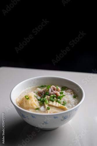 Bowl of hot Asian pork congee rice porridge on dark background.