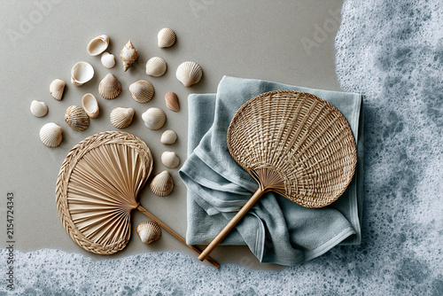 Scattered seashells and woven fans on a towel beside sea foam