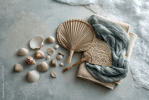 Woven fans and seashells scattered beside a linen towel and sea foam