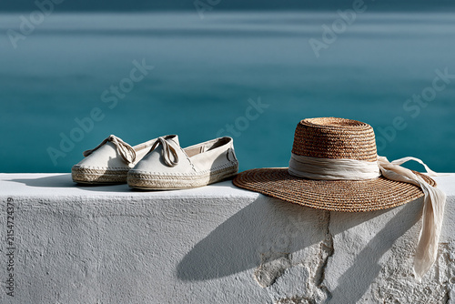 Canvas espadrilles and a woven sun hat resting on a wall above the sea