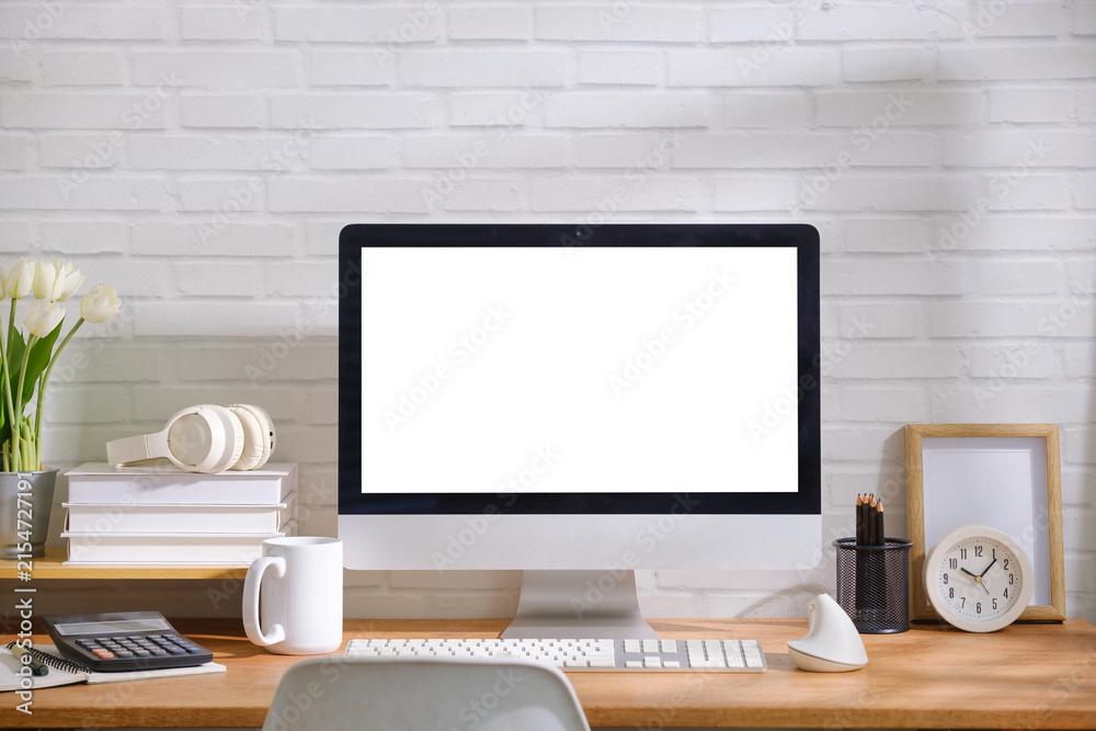 Fototapeta premium Modern office desk setup with desktop computer mockup, keyboard, mouse, calculator, coffee mug and stationery on a wooden table against a white brick wall.