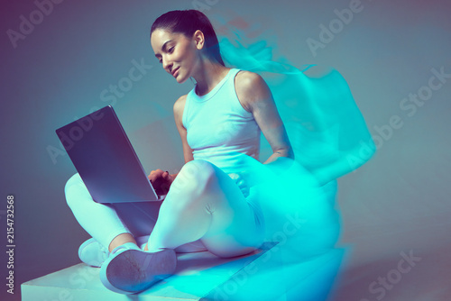 Young pretty girl freelancer sitting with laptop working remotely in neon studio light. Freelance work. Long exposure