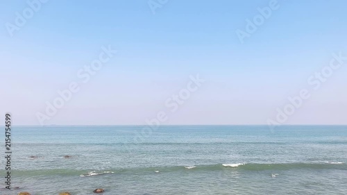 Calm blue sea waves rolling towards rocky shore under clear sky