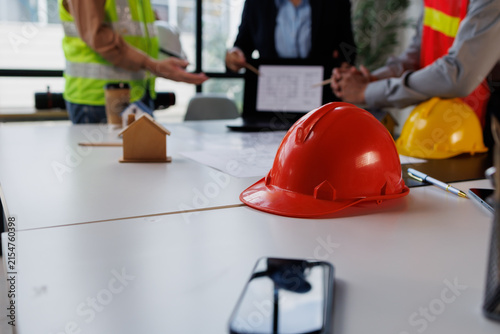 Construction team collaborating on building project, discussing blueprints and property development with safety hardhats on table